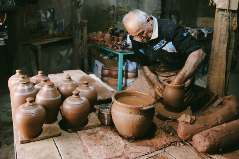 Senior man handcrafting pottery jugs in a traditional workshop, showcasing skilled craftsmanship.