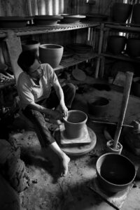 Black and white image of a potter skillfully shaping a clay vessel in a rustic workshop.